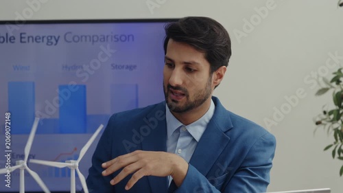 Portrait of Latin engineer demonstrates work of wind turbines in boardroom. Hispanic sustainable power professional conducts conference in office. Green energy