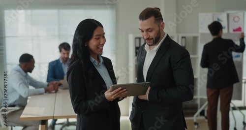 Portrait of Asian businesswoman speaks with bearded Middle Eastern manager as holds tablet in office. Man listens closely and discusses project details