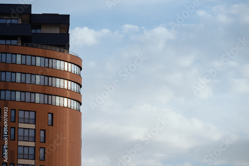 Modern residential apartment building facade with a unique curved wall against a blue cloudy sky backdrop with large copy space . Geometric composition of modern urban corporate architecture 