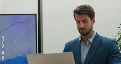 Portrait of Hispanic man entrepreneur uses laptop to analyze financial data in office. Latin American bearded manager compares information online in workplace