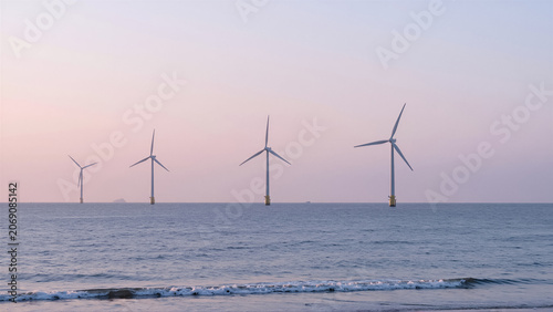 Offshore wind turbines stand tall in the calm ocean under a beautiful pastel sky at dusk. This serene scene symbolizes sustainable power generation and a commitment to clean energy for th