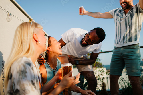 Diverse friends laughing and enjoying a rooftop party with beer