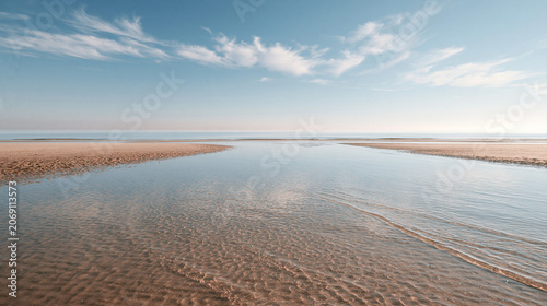 Картината върху платно Golden hour light stretches across a calm sandy shore near the water