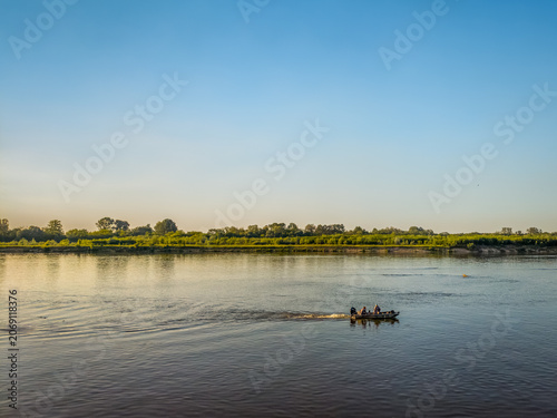 Принти на полотні A wide landscape view of a small fishing boat cruising along the peaceful Vistula River in Poland during a bright summer afternoon