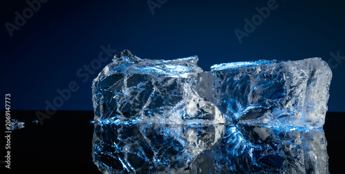 Tableau sur toile Broken ice with blue backlight on a black reflective background.