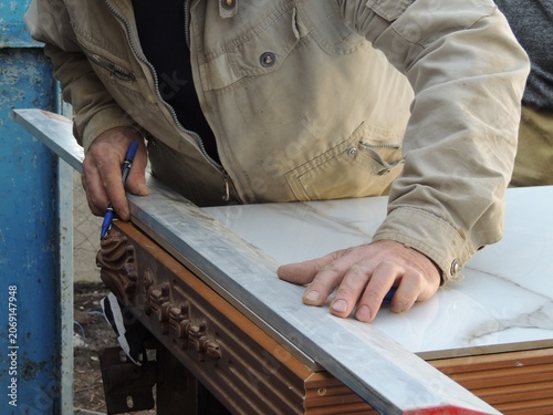he process of marking large-format tiles before cutting them. The tiler presses a long aluminum construction straightedge against the surface of the tile and makes markings.