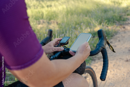 Cyclist checking smartphone and cycling computer navigation on gravel route