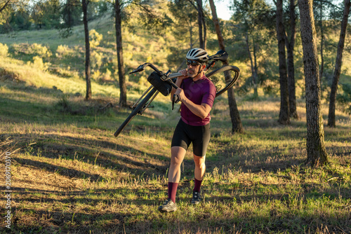 Cyclist carrying bicycle walking through forest gravel path