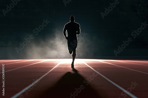 Silhouetted athlete sprints down a track, bathed in dramatic light and fog