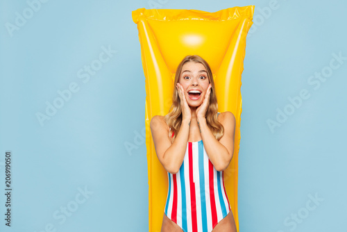 Young shocked surprised woman wear bikini striped swimsuit rest lies on inflatable mattress hotel pool put hand on face isolated on plain pastel blue background. Summer vacation sea sun tan concept.