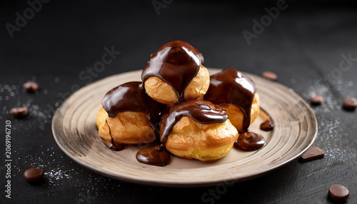 Cream Filled Profiteroles Topped With Rich Chocolate Sauce Sit On Dark Moody Background Creating Tempting And Indulgent Dessert Scene