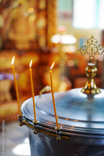 Orthodox baptism font with burning candles and golden cross closeup vertical