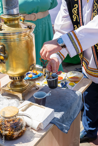 Pouring hot tea from a traditional brass samovar at a folk festival.
