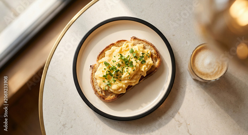 Scrambled eggs on toasted sourdough bread with fresh chives next to coffee cup on table