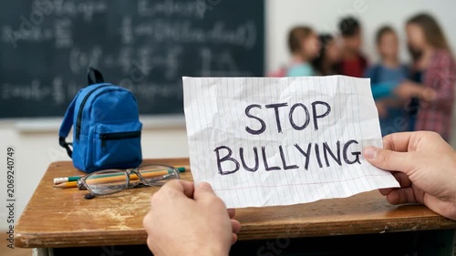 Student holding stop bullying message in classroom, raising awareness about harassment and peer pressure among students