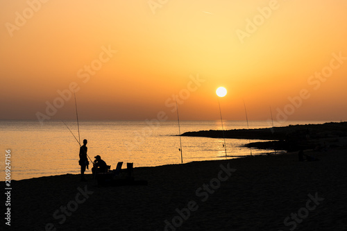 Fiery Sunset with Fishermen Silhouettes on the Beach at San Pietro in Bevagna, Puglia, Italy