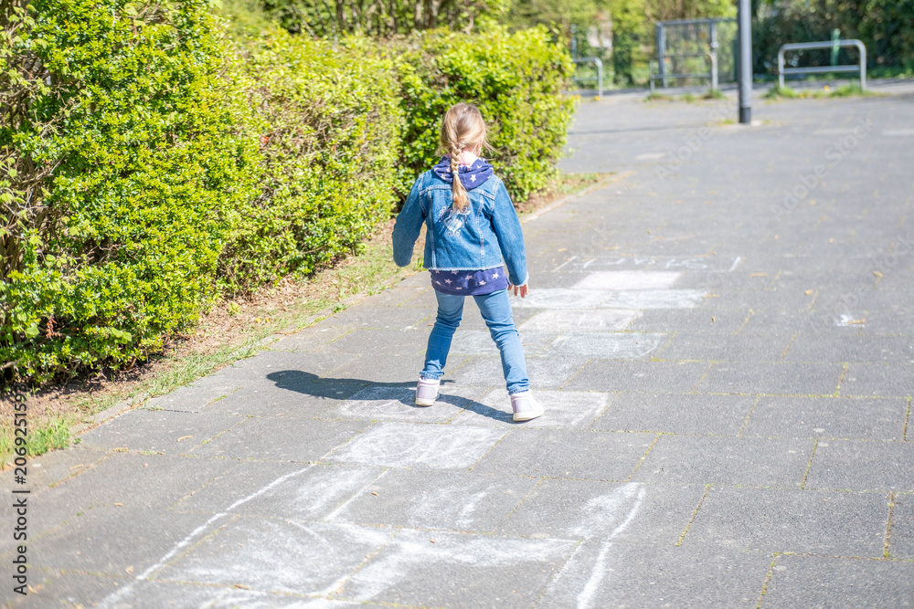 Fototapeta premium Child playing hopscotch on sunny day, legs of a girl in jeans and sneakers jumping on chalk squares on pavement, active outdoor traditional games, childhood fun, back to school leisure, happy girlhood