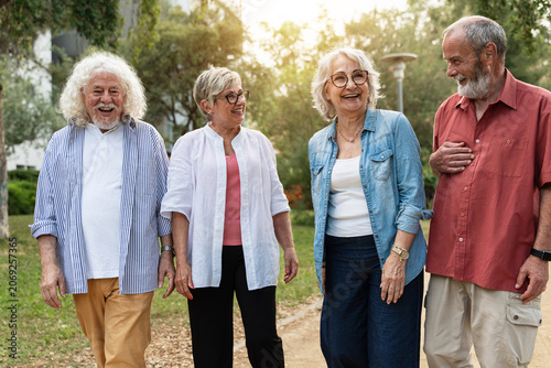 Happy senior friends walking together in public park enjoying fun conversation during retirement