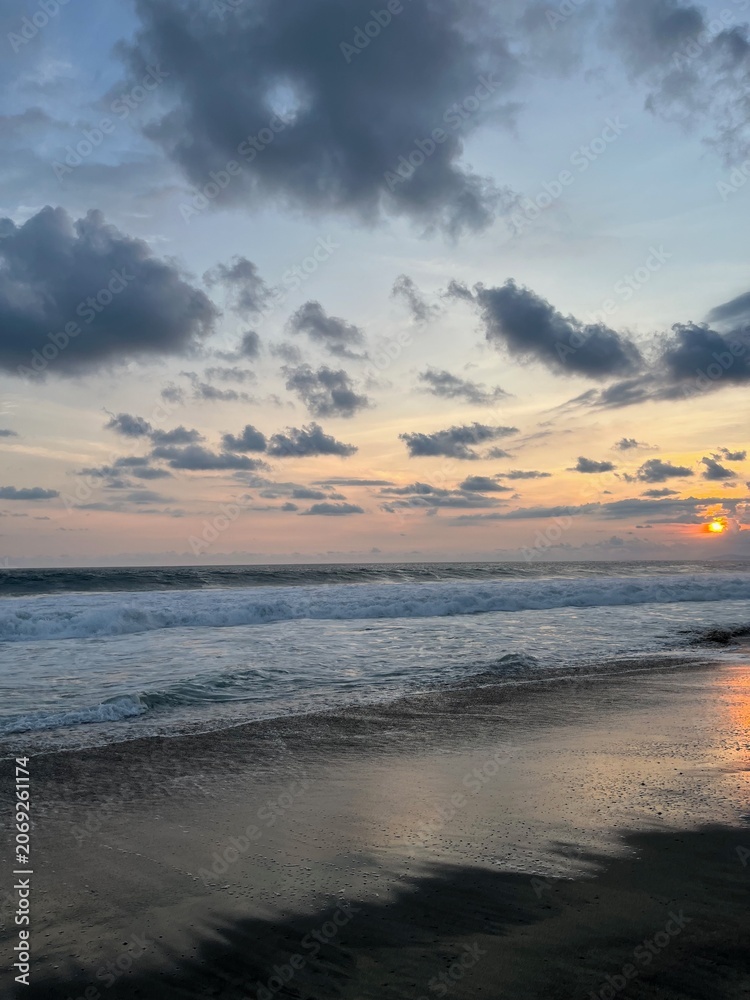 Fototapeta premium Dramatic ocean sunset with bright sun glowing at the horizon and reflecting on wet beach