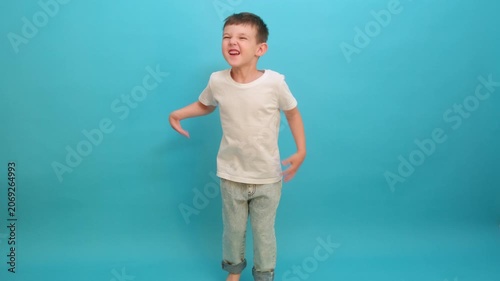 Happy child boy jumping against blue background. Joyful kid in white t-shirt having fun, active lifestyle and childhood energy. Concept of activity, movement and playful emotion.
