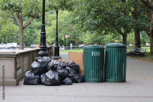 Outdoor scene with trash bags, containers, and boxes, next to a sidewalk and park