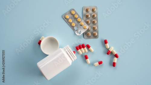 Photos A flat lay of a white pill container with scattered red and white capsules alongside silver blister pack medication strips on a light background