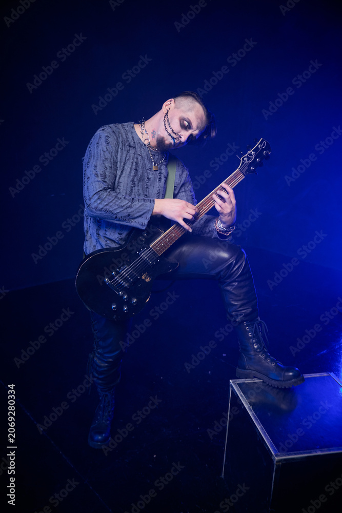 Fototapeta premium Adult male musician with skeletal face paint playing electric guitar in blue stage lighting