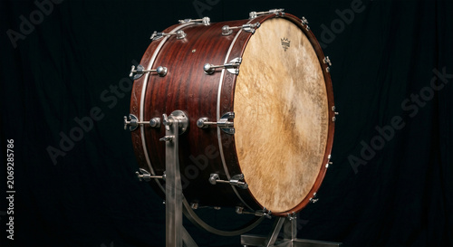 A professional product photograph of a modern concert bass drum suspended in a tilting cradle stand, positioned against a seamless, matte-black background 