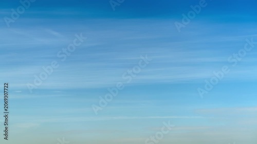 Blue sky with light wispy clouds spanning the horizon, time lapse. Clear weather background with soft texture. Natural atmosphere for inspirational design, freedom concept and outdoor scenery view.