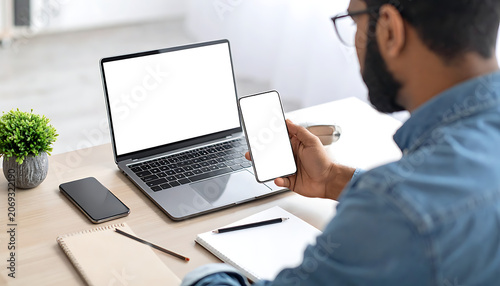 Man using laptop and smartphone for remote work, working from home, with blank screens for copyspace and digital communication