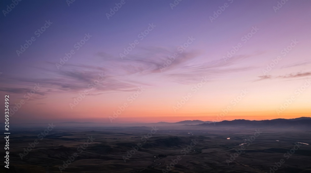 Fototapeta premium Vibrant Sunset Sky Over Rolling Hills and Distant Mountains.