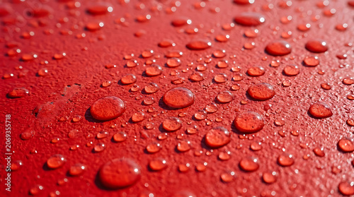 Close-up view of water droplets scattered on a vibrant red painted surface capturing intricate textures and reflections