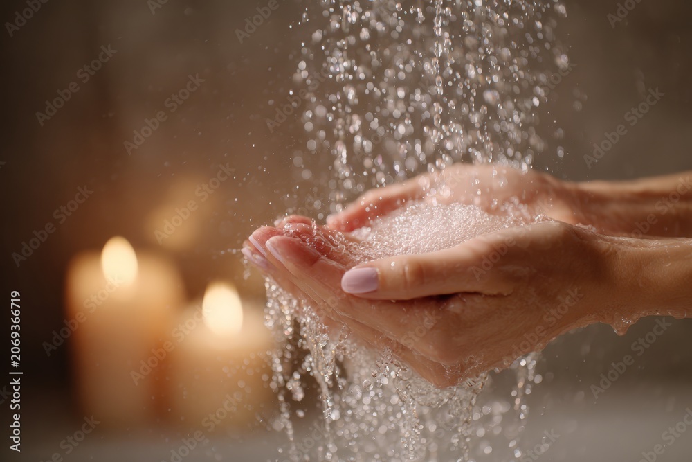 Fototapeta premium Close up of manicured hands under warm shower stream with candlelight for spa background and soothing wellness banner