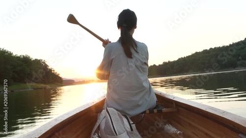 Rear view of female canoeing across lake at dusk