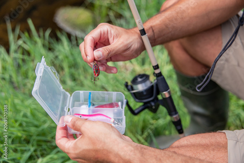 Fisherman selecting fishing lure from tackle box near river