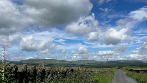 Car POV driving downhill in picturesque Lancashire countryside, rider approaching. Narrow country lane framed by stone walls, Gisburn Forest further down.