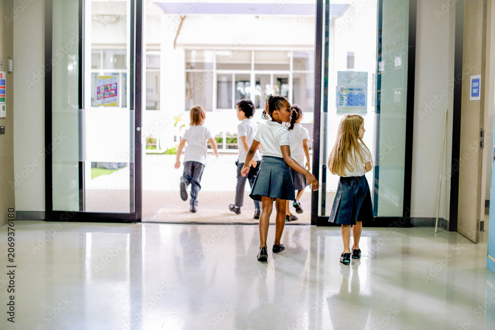 Fototapeta premium Children in school uniforms walking through a bright hallway.
