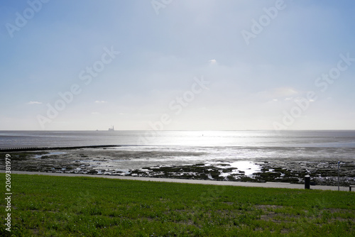 A picturesque view from the grassy beach at Friedrichskoog of the incoming tide in the Wadden Sea, with beautiful reflections of the sun on the water's surface.
