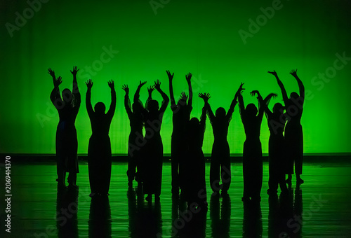 Dancers silhouetted on stage raising hands in unity
