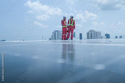 Billede på lærred On-site view as pair of technicians in red protective suits stride across rows of photovoltaic panels on a city rooftop, capturing green technology, renewable energy and engineering