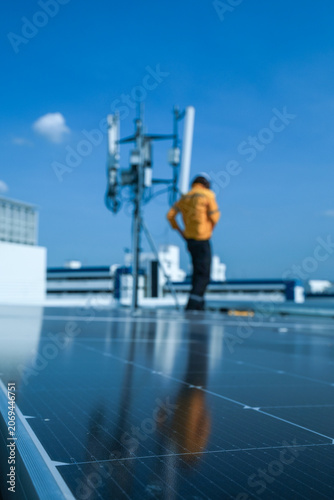 On-site view as a field technician in a yellow safety jacket stands by a 5G antenna on the building roof atop a commercial building, capturing sustainable power, solar power generation.