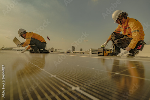 A field engineer in a yellow safety jacket carries out repairs on a solar module on the rooftop against the Bangkok skyline, showing renewable energy, inspection and maintenance.