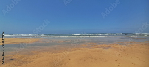 Empty sandy beach with calm ocean waves and blue sky