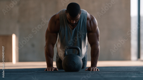 Kettlebell coach filming an instructional video in a quiet morning gym before clients arrive, demonstrating a Turkish get-up in careful deliberate segments, only the sound of