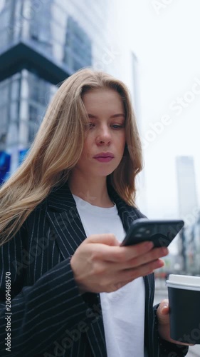 Young woman checking smartphone while holding coffee during urban commute