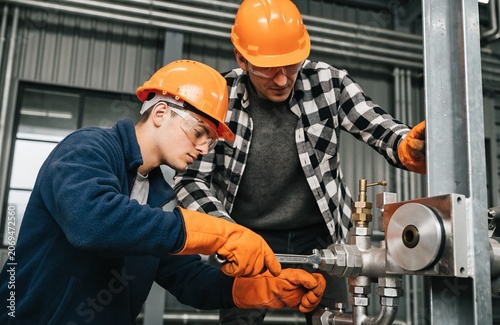 Two Male Workers Repairing Industrial Pipe System With Wrench In Factory For Manufacturing Concepts