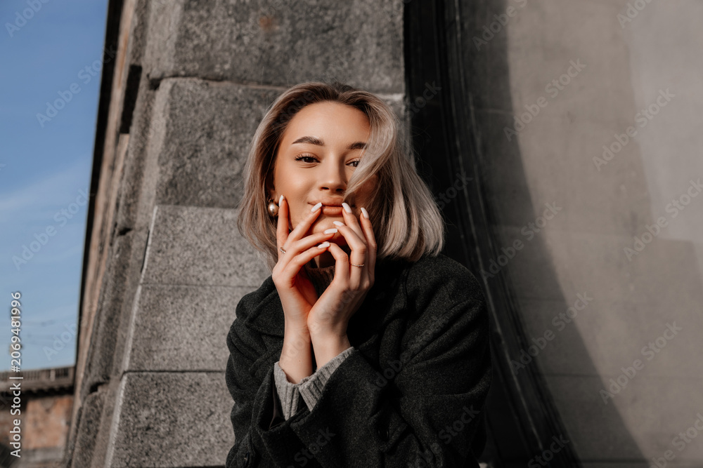 Obraz premium Young woman in stylish dark coat standing on Vltava river embankment in Prague. Elegant winter urban portrait, European architecture, cold season, travel and city lifestyle, authentic everyday moments
