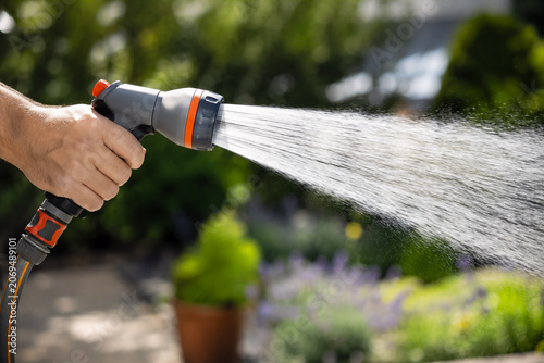 Modern Garden Hose Nozzle Spraying Water on Sunny Summer Day, Close-Up with Shallow Depth of Field