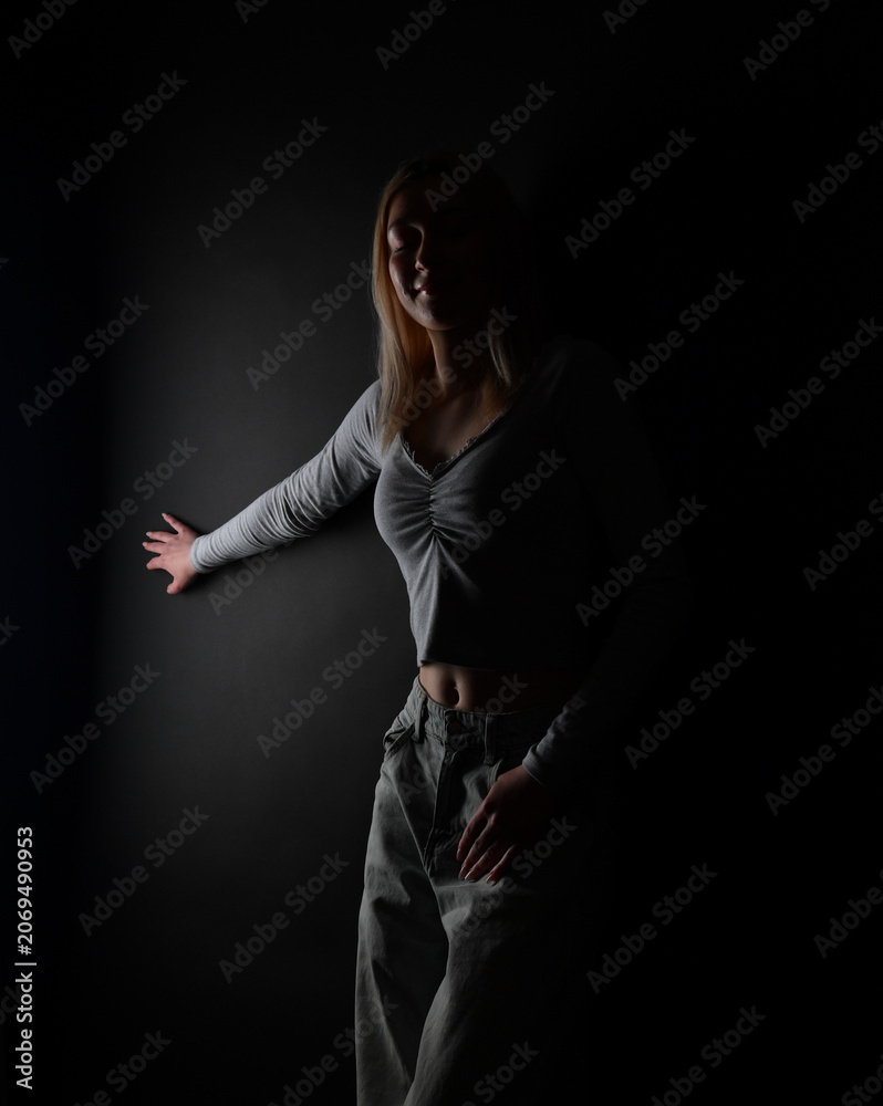 Fototapeta premium Junge Frau in dunkler Low-Key-Beleuchtung. Emotionales Porträt für Selbstreflexion, mentale Gesundheit, Einsamkeit, Hoffnung, Persönlichkeit und innere Stärke.