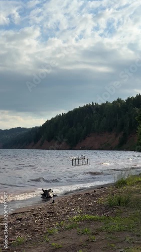 Shoreline of reservoir after storm with clouds and wooden dock. Mobile vertical video 